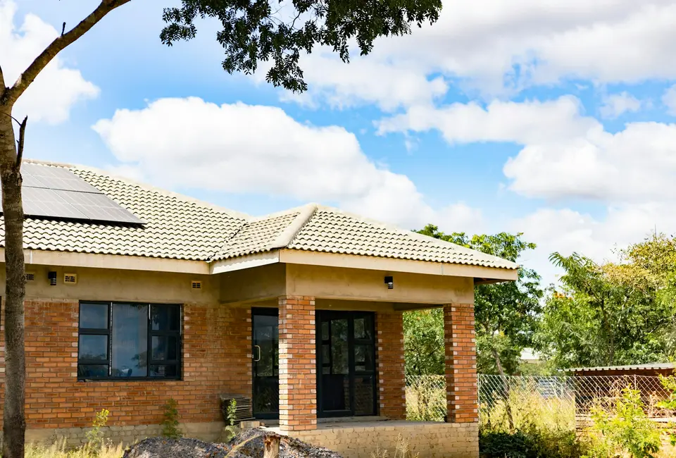 A single-storey brick house with a tiled roof and rooftop solar panels under a blue sky